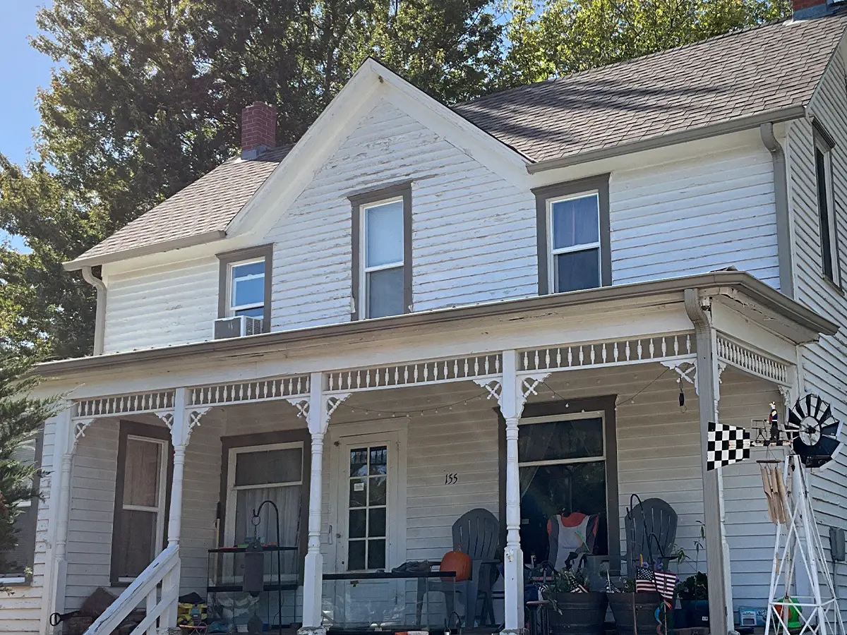 Original view of a two-story vintage home before updates, featuring worn exterior details and a cluttered front porch