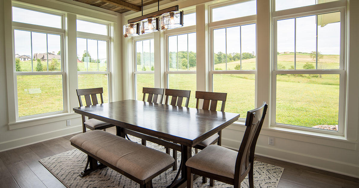 A rustic dining space featuring a wooden ceiling, large double-hung windows, and scenic countryside views.