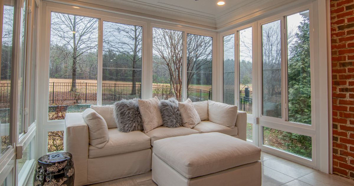 Cozy sunroom with floor-to-ceiling windows, a plush sectional sofa, and scenic backyard views, perfect for natural light.