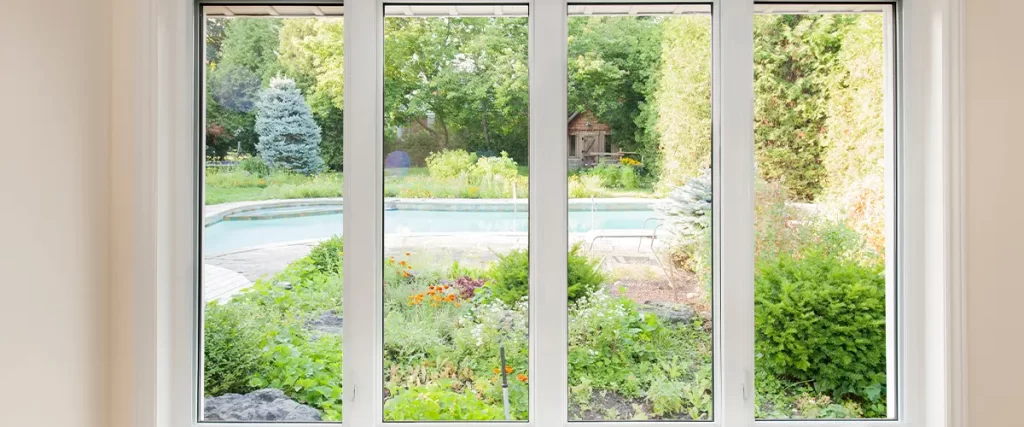 Large picture windows with a view of a backyard pool and garden