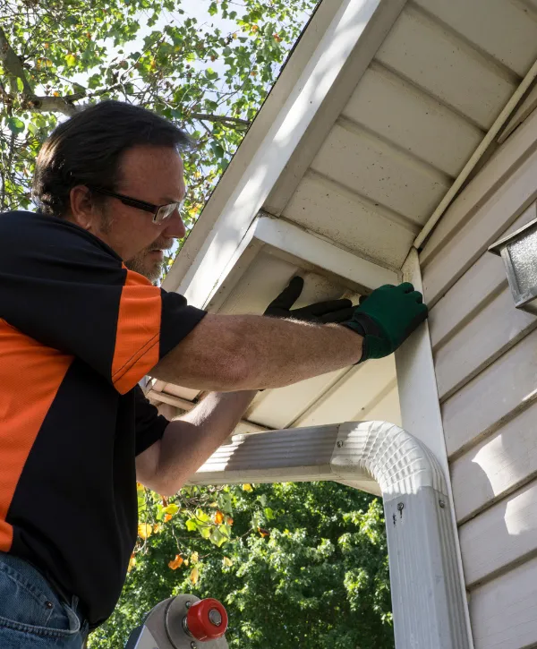 A man wearing gloves and safety glasses installing or repairing the soffit and fascia on a house