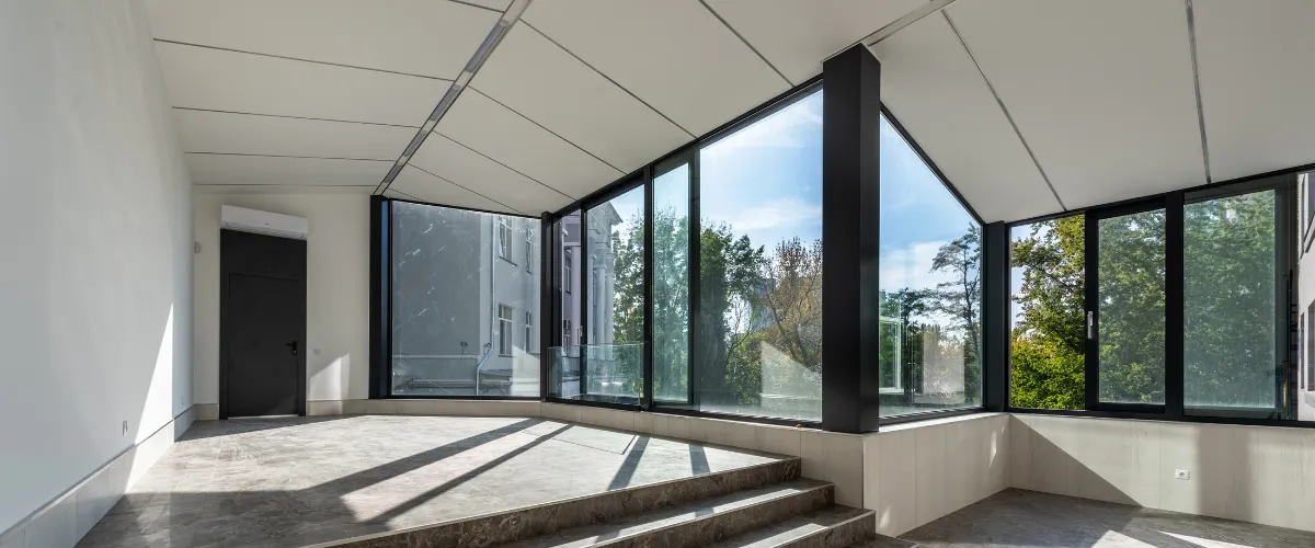 Spacious modern glass room with large windows, marble flooring, and a sleek black frame design.