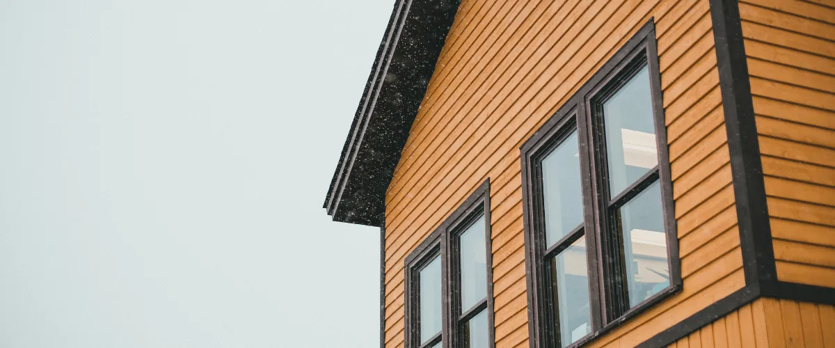 A contractor on scaffolding using a measuring tape to install soffit and siding on a house