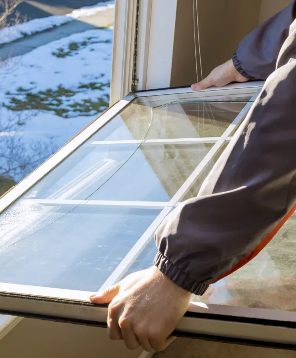 A person removing a cracked window pane from a frame on a cold winter day.