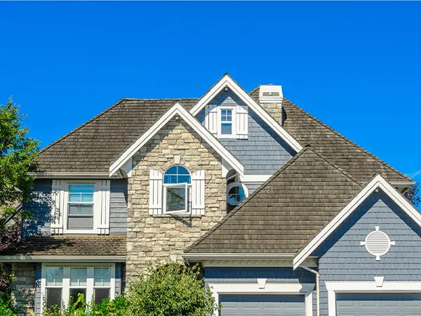 Beautiful suburban home with a stone and shingle facade featuring a well-maintained asphalt shingle roof