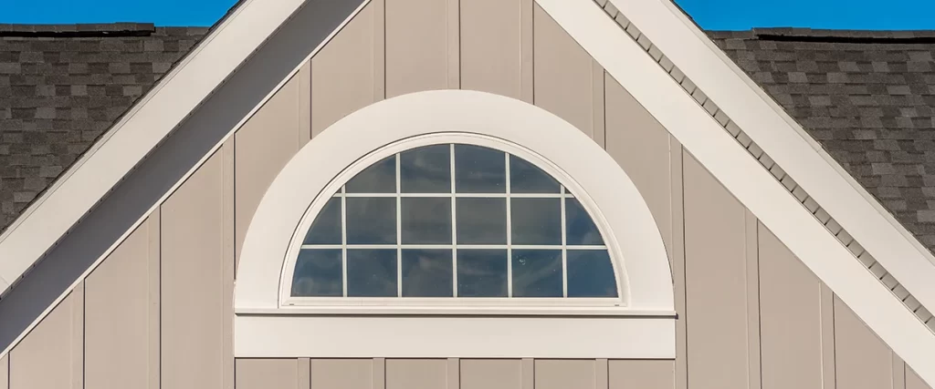 alf-round attic window with white grille set in gabled vinyl siding exterior