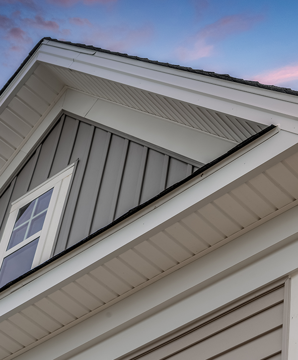 Modern house with professional siding installation featuring gray vertical panels, white trim, and fitted gutters highlighted by a vibrant sunset sky