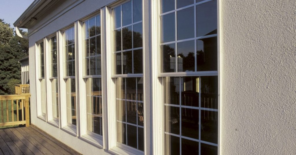 Row of large white casement windows installed on a home exterior overlooking a wooden deck.