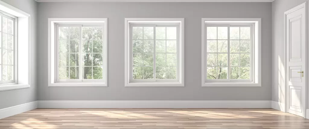 Empty room with grey walls and wood flooring featuring three identical white sliding windows.
