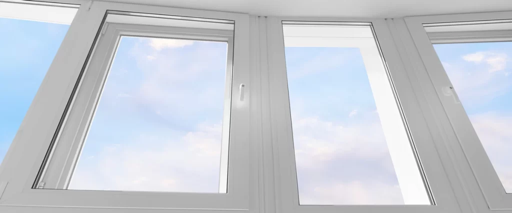 Upward angle view of clean white vinyl window frames looking out into a clear blue sky with soft white clouds, showcasing energy-efficient residential window design.