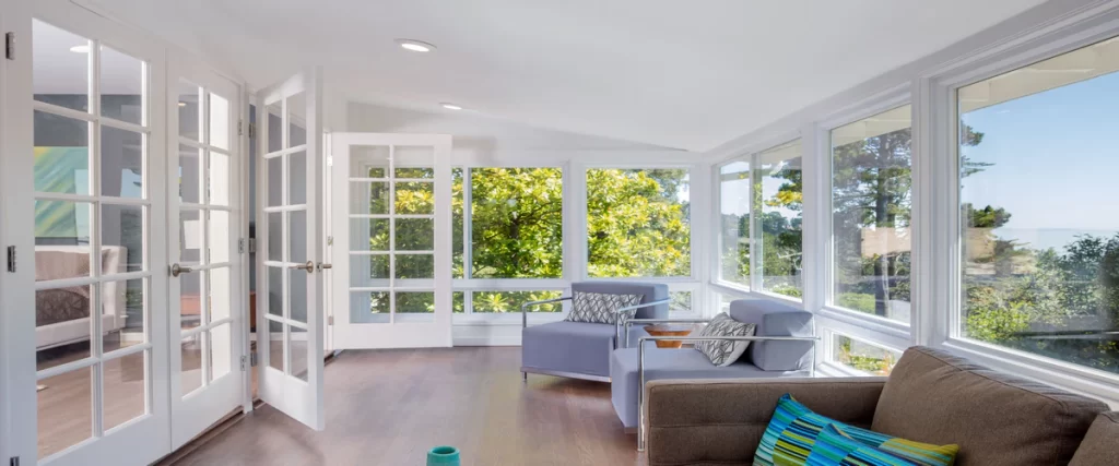 A bright and spacious sunroom featuring floor-to-ceiling ProVia Aspect vinyl windows and white French doors overlooking a lush green garden.