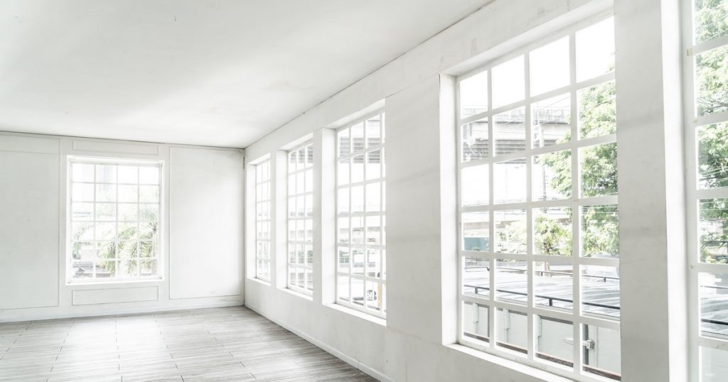 A bright, minimalist room featuring a wall of white multi-pane windows, highlighting the design differences when considering ProVia vs Pella windows for a home renovation.