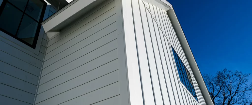 Newly installed white LP SmartSide siding showing a combination of horizontal lap and vertical board and batten styles against a clear blue sky.